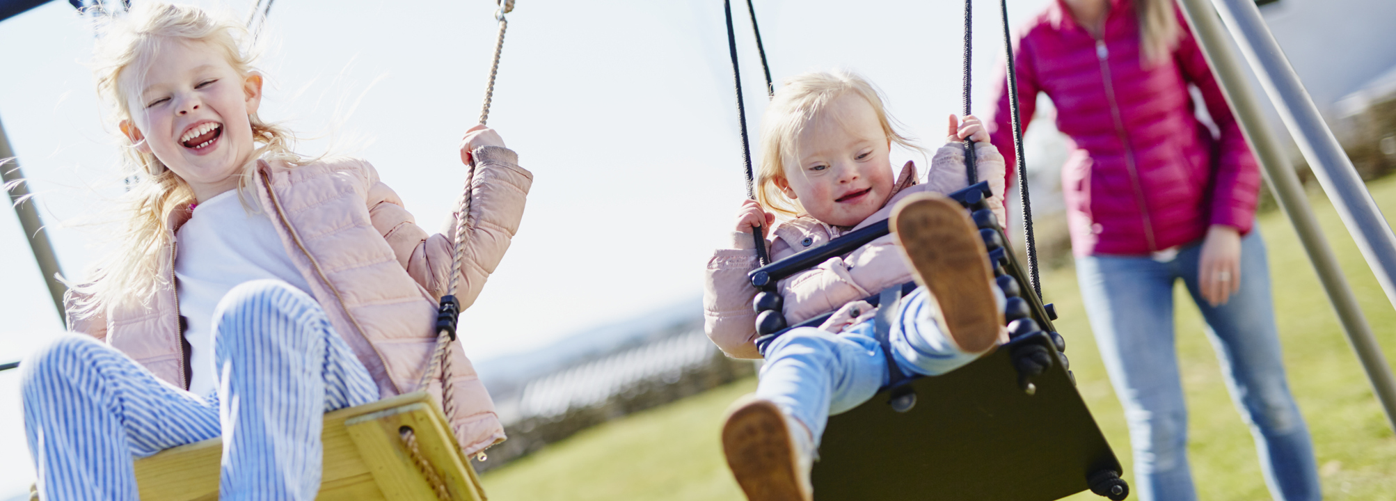Två barn gungar i lekpark med sin mamma.